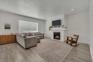 Living area featuring a glass covered fireplace, light wood finished floors, baseboards, recessed lighting, and a textured ceiling