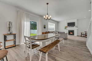 Dining space with light wood-style flooring, a glass covered fireplace, a chandelier, and baseboards