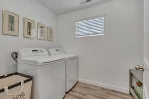 Washroom featuring washing machine and dryer, light wood-style flooring, and baseboards