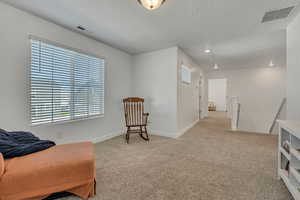 Living area featuring healthy amount of natural light, carpet flooring, an upstairs landing, baseboards, and a textured ceiling