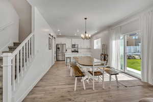 Dining area with a barn door, light wood-style flooring, a chandelier, recessed lighting, and stairway