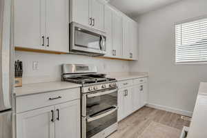 Kitchen featuring appliances with stainless steel finishes, light wood-type flooring, light countertops, white cabinetry, and baseboards