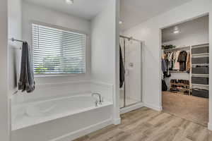 Bathroom featuring a shower stall, a garden tub, a walk in closet, and wood finished floors