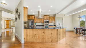 Kitchen with appliances with stainless steel finishes, island exhaust hood, light wood finished floors, baseboards, and recessed lighting