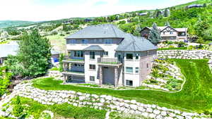 Rear view of property featuring a balcony, stucco siding, and stone siding