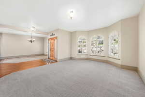 Spare room featuring light colored carpet, a chandelier, and baseboards