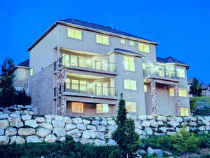 Rear view of house with stucco siding, a balcony, and stone siding