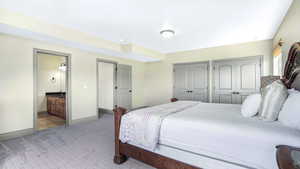 Bedroom with multiple closets, light colored carpet, baseboards, and ensuite bath