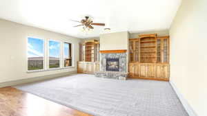 Unfurnished living room featuring a ceiling fan, baseboards, a stone fireplace, light colored carpet, and light wood-style floors