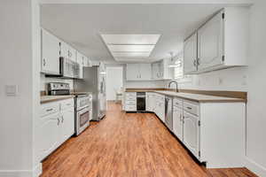Kitchen featuring stainless steel appliances, light wood-style flooring, a sink, white cabinetry, and light countertops