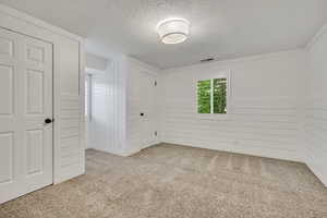 Unfurnished bedroom featuring a textured ceiling, carpet flooring, a closet, and wooden walls