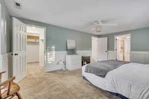 Carpeted bedroom with a spacious closet, wainscoting, a closet, a ceiling fan, and ensuite bath