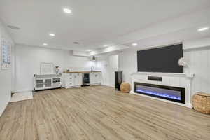 Unfurnished living room featuring wine cooler, light wood-style floors, a sink, a glass covered fireplace, and recessed lighting