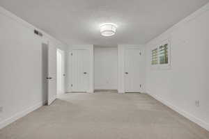 Empty room featuring a textured ceiling, light colored carpet, and baseboards