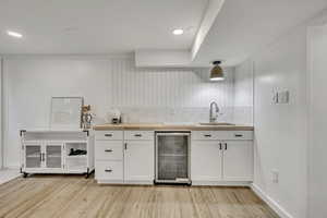 Kitchen featuring wine cooler, a sink, butcher block countertops, light wood-style floors, and white cabinetry