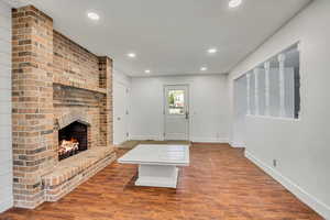 Unfurnished living room featuring recessed lighting, baseboards, a brick fireplace, and wood finished floors