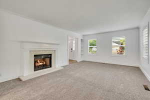 Unfurnished living room with a high end fireplace, ornamental molding, carpet flooring, and baseboards