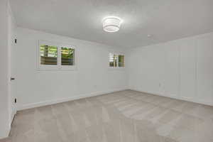 Unfurnished room featuring a textured ceiling, light carpet, and a decorative wall