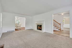 Unfurnished living room featuring carpet, crown molding, stairs, a chandelier, and a fireplace