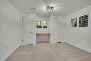 Unfurnished bedroom featuring light colored carpet, a textured ceiling, wood walls, and baseboards