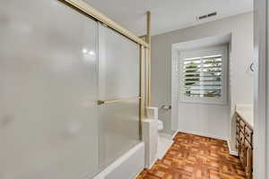 Full bathroom featuring vanity, toilet, bath / shower combo with glass door, and baseboards