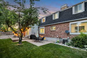 Back of house at dusk with a shingled roof, mansard roof, brick siding, central AC, and a patio area