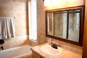 Bathroom with a tub with jets, vanity, and wallpapered walls