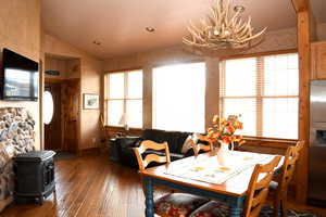 Dining space featuring vaulted ceiling, hardwood / wood-style flooring, a wood stove, baseboards, and a chandelier