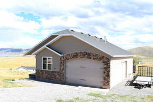 View of front facade featuring stone siding, a mountain view, a garage, and gravel driveway