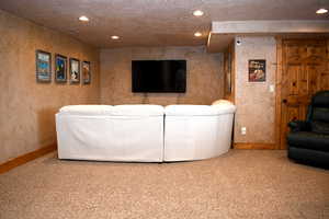 Carpeted living room featuring baseboards, recessed lighting, a textured ceiling, and a textured wall