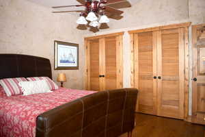 Bedroom featuring multiple closets, dark wood-style floors, wallpapered walls, and a ceiling fan