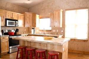 Kitchen with appliances with stainless steel finishes, light brown cabinetry, light wood-type flooring, a kitchen island, and wallpapered walls