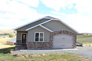 View of front of home with stone siding, an attached garage, and gravel driveway