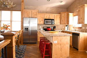 Kitchen with stainless steel appliances, light brown cabinets, a center island, and hardwood / wood-style floors