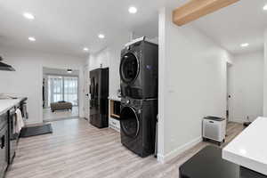 Kitchen featuring stacked washer / drying machine, black fridge, white quartz countertops, light gray flooring, and recessed lighting