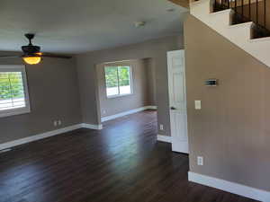 Spare room with dark wood-style flooring, a smoke detector, baseboards, ceiling fan, and stairs