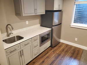 Kitchen with appliances with stainless steel finishes, a sink, gray cabinetry, dark wood finished floors, and light countertops