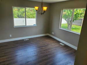 Empty room with a chandelier, dark wood finished floors, and baseboards