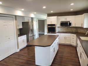 Kitchen featuring stainless steel appliances, dark countertops, a sink, dark wood-type flooring, and recessed lighting