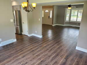 Empty room featuring a ceiling fan, a chandelier, baseboards, and dark wood-type flooring