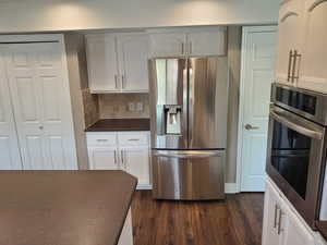 Kitchen with appliances with stainless steel finishes, dark countertops, dark wood-style flooring, decorative backsplash, and white cabinets