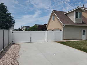 View of side of home with a gate, a shingled roof, and concrete driveway