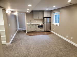 Kitchen with appliances with stainless steel finishes, dark carpet, baseboards, gray cabinetry, and recessed lighting