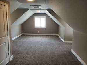 Bonus room with carpet, a textured ceiling, lofted ceiling, and baseboards