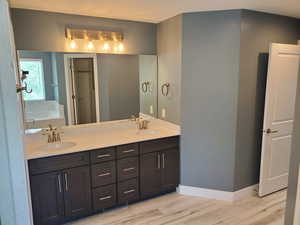 Full bathroom featuring double vanity, wood finished floors, a garden tub, and baseboards