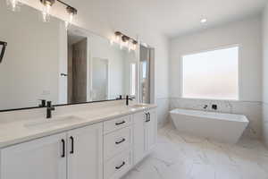 Full bathroom with double vanity, a soaking tub, marble finish flooring, recessed lighting, and wainscoting