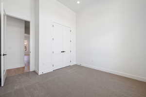 Unfurnished bedroom featuring carpet, baseboards, a closet, recessed lighting, and a towering ceiling