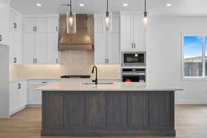 Kitchen featuring oven, island exhaust hood, a sink, decorative backsplash, and light wood-style floors