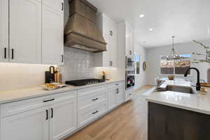 Kitchen with premium range hood, stainless steel appliances, light wood finished floors, white cabinets, and recessed lighting