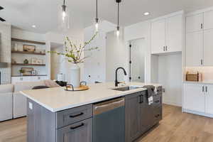 Kitchen with dishwashing machine, light wood-style floors, white cabinets, light countertops, and a kitchen island with sink
